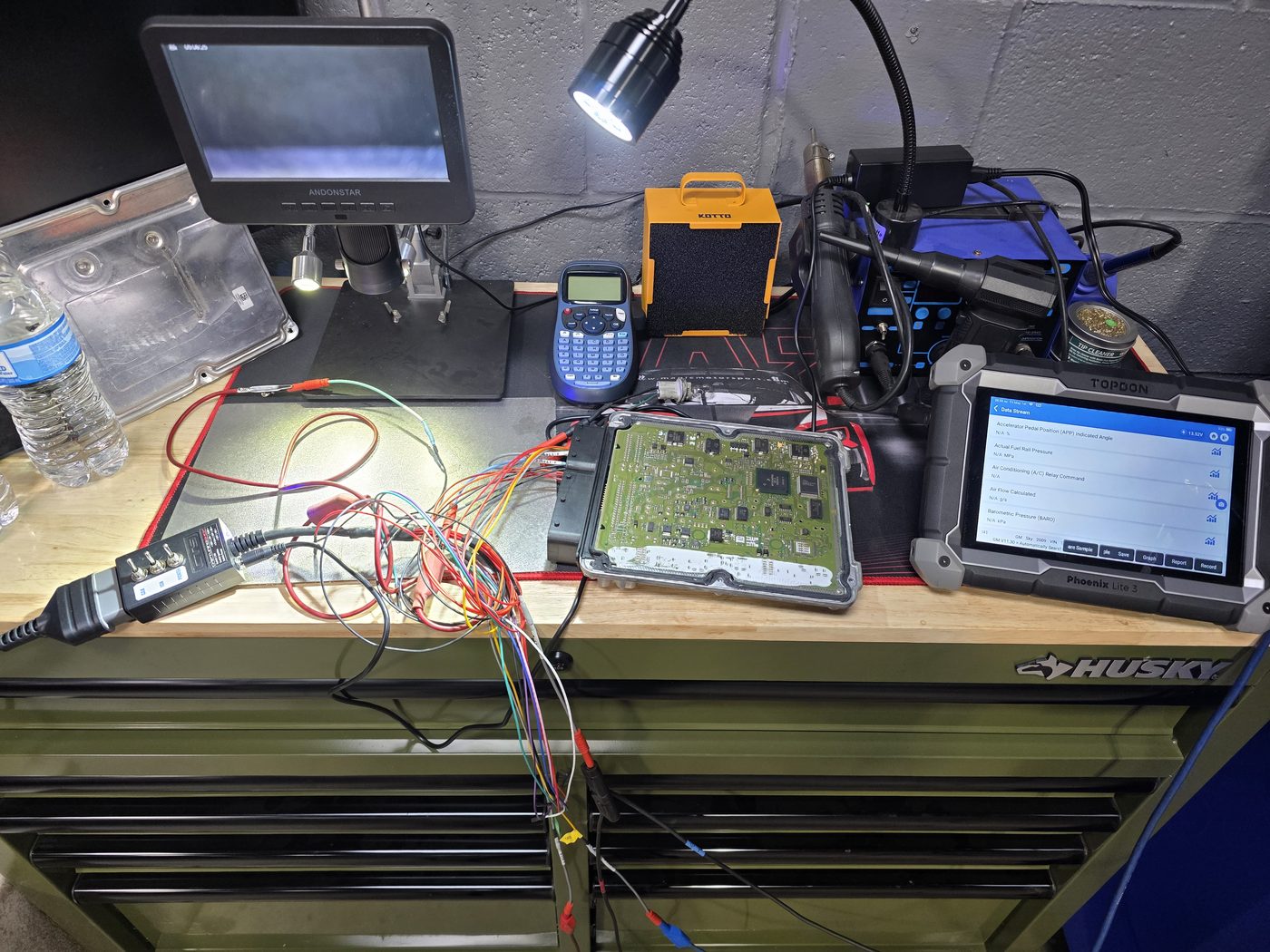 ECU circuit board on the bench with breakout leads and diagnostic scan tablet during board-level repair